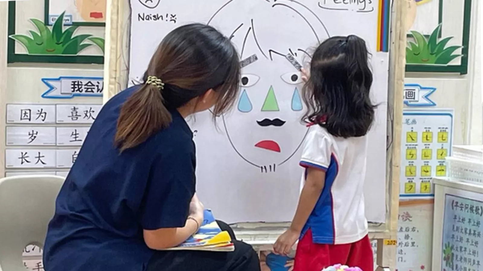 An educator guides a child in a whiteboard activity, using paper cut-outs to illustrate emotions and learn self-regulation.