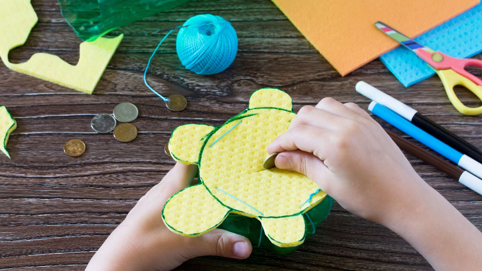 A child inserts a coin into a handmade piggy bank, showcasing a fun craft for children that also teaches good saving habits.