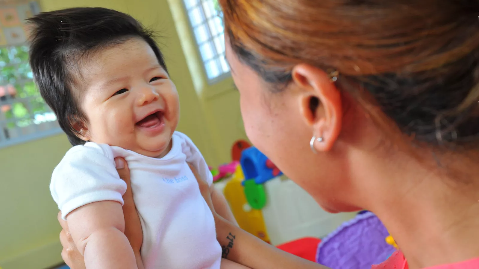 A woman smiles and gently cradles a baby in her arms, setting an optimal emotional climate for the child’s development.