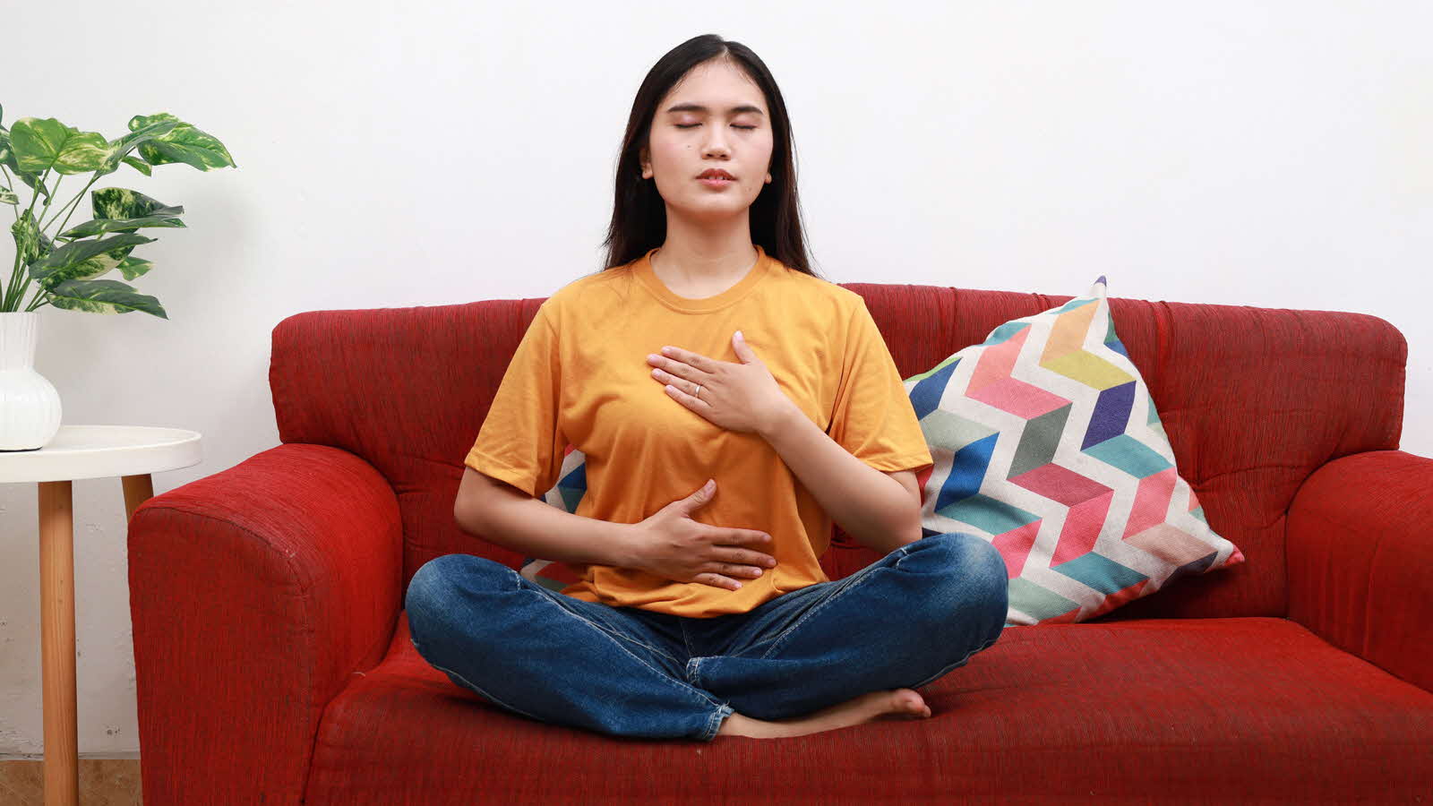 A woman sits cross-legged on a couch and practises anchor breathing, a good way to stay calm and be more mindful at work.