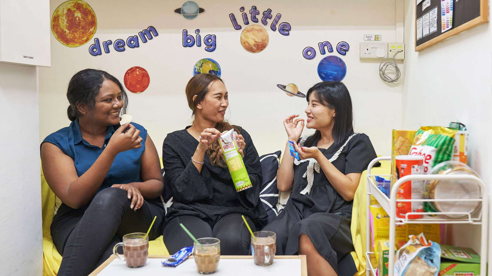 Educators-Ask-The-Experts-Mindfulness-and-well-being-MAIN Three preschool educators sit on a couch, happily sharing snacks and enjoying each other’s company.