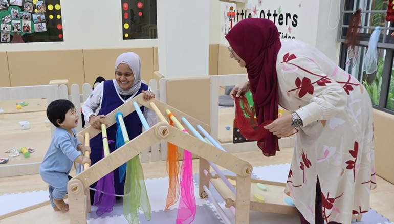 Two educators engaging an infant climbing the open-ended gym set.