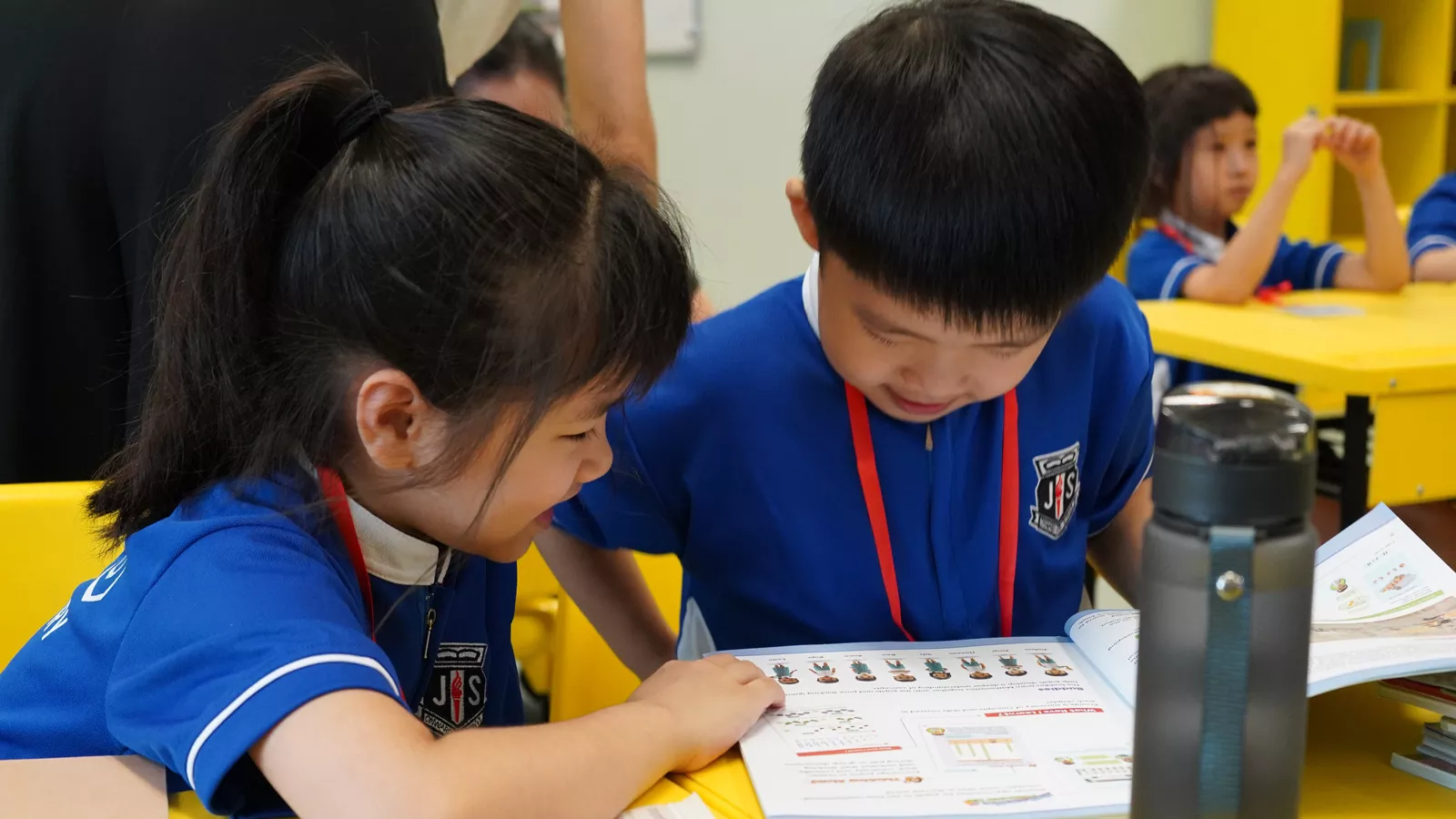 Two Primary 1 children are focused on a book in class, symbolising their successful transition to formal schooling.