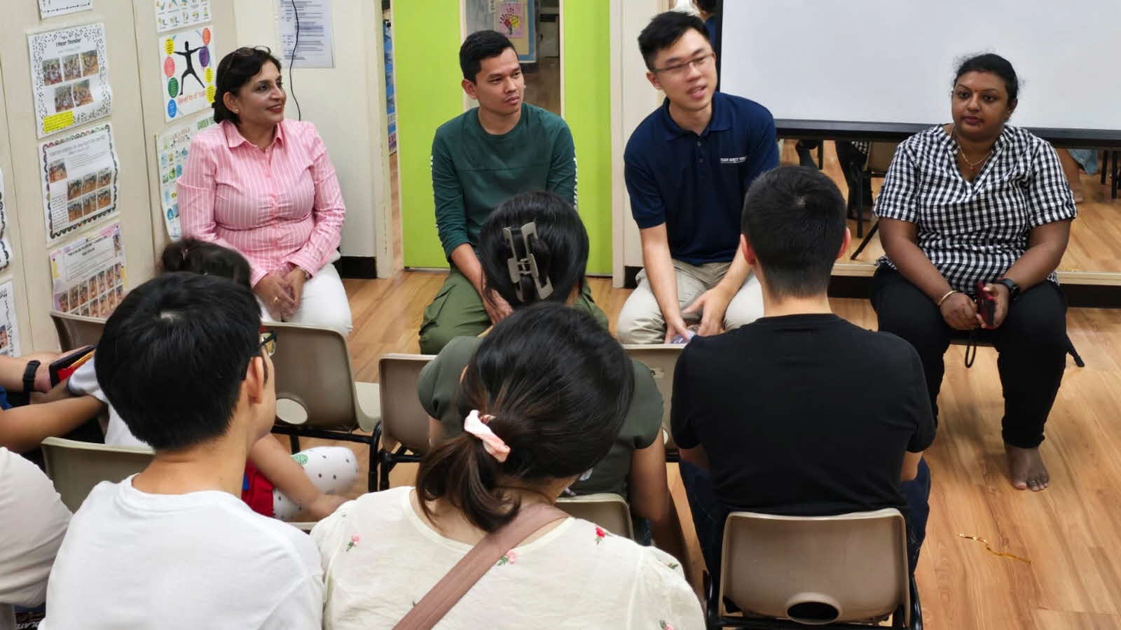 Several individuals, including principal Sumitra Tiwari, sit in chairs and face other parents, engaged in two-way dialogue.