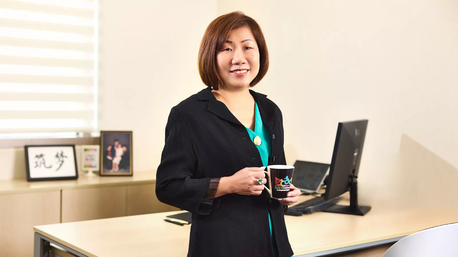 Ku Geok Boon holds an ECDA mug while standing in her office.