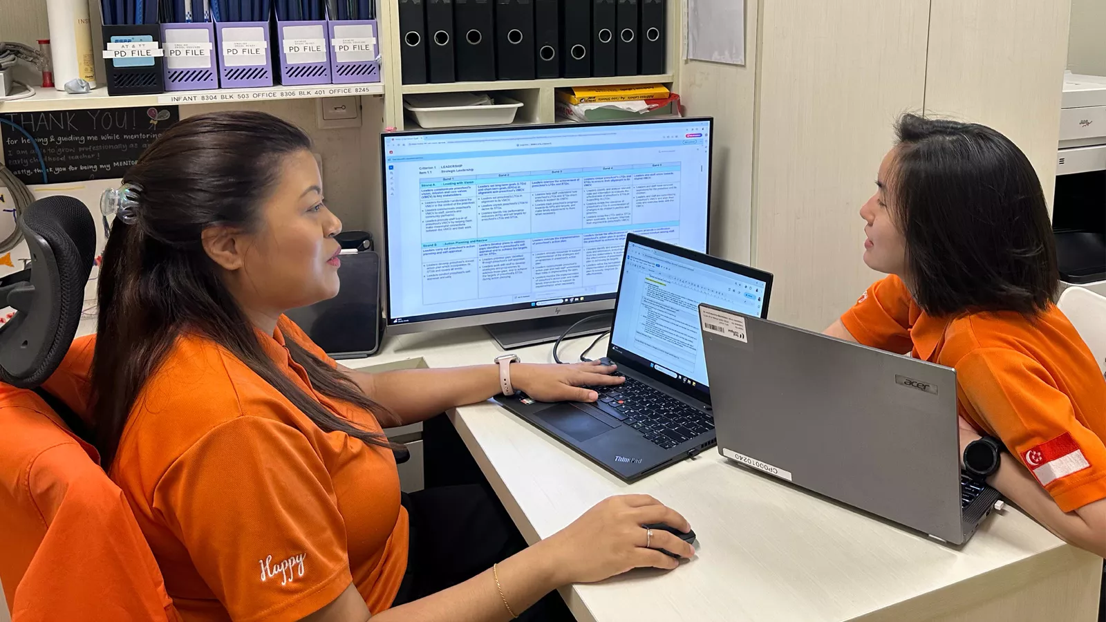 Centre principal Siti Daliana and a colleague sit at a desk, discussing ways to improve preschool quality.