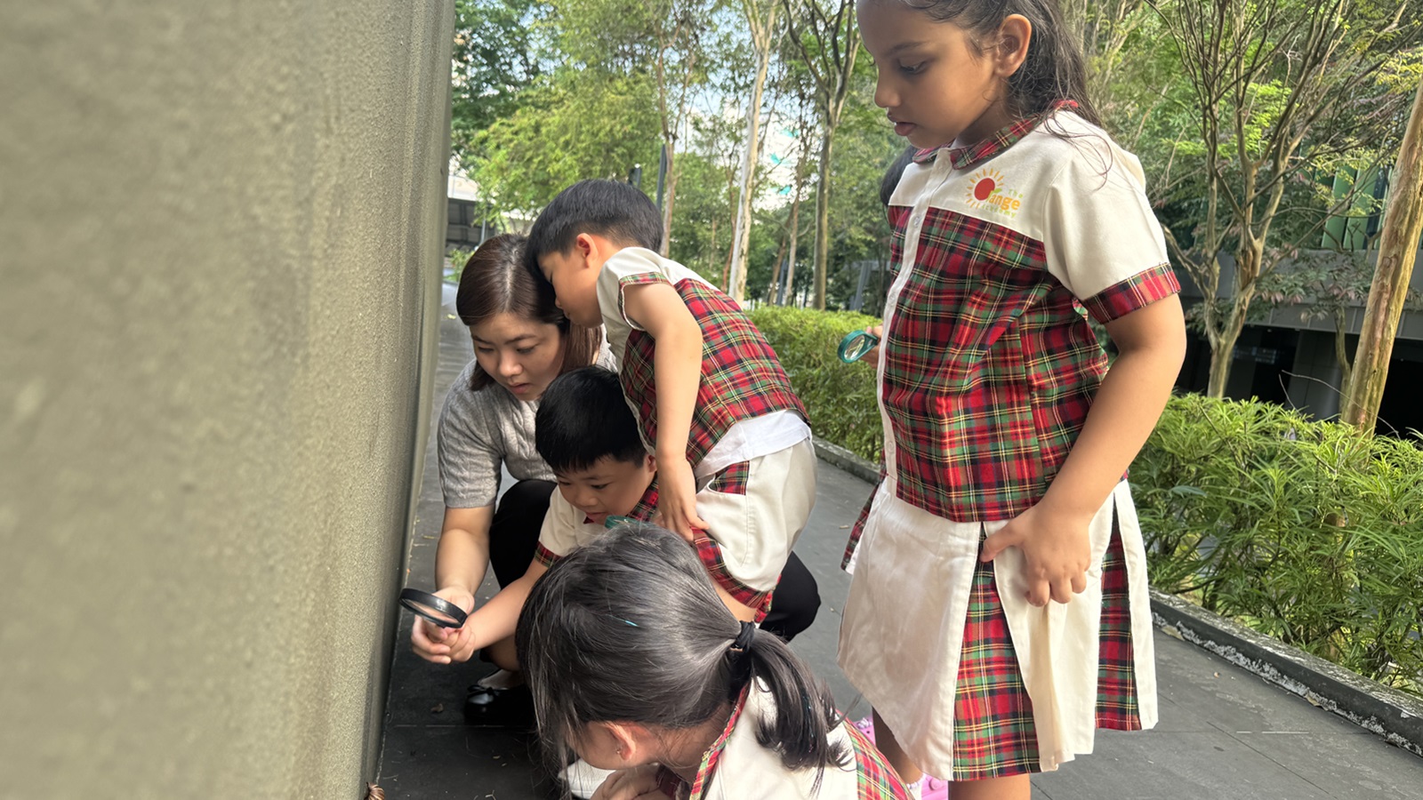 Educator and a group of children looking at a snail with a magnifying glass outdoors
