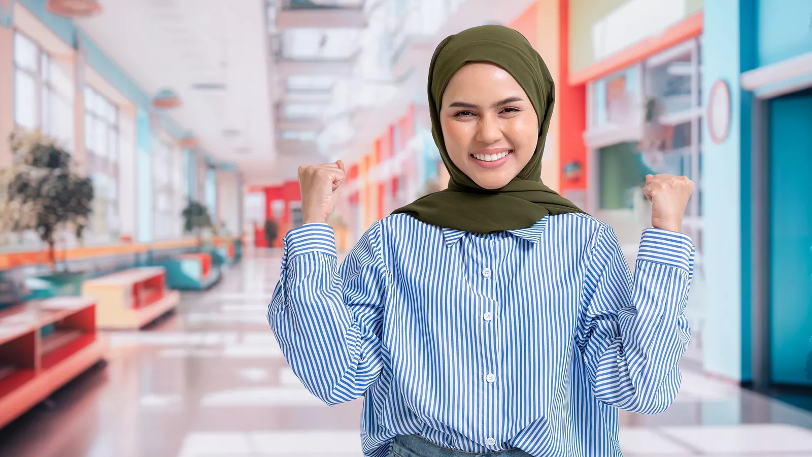 A woman smiles brightly while pumping her fists, in a gesture of courage and clarity, against a school backdrop.