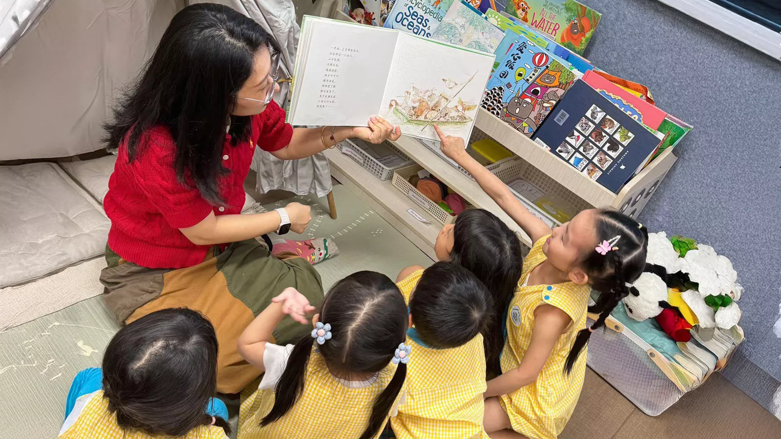 Educator Miao Dan reads a Chinese storybook to a group of attentive children sitting around her.