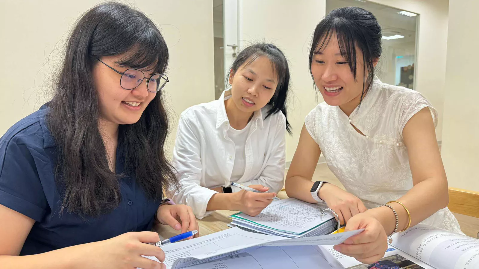 Educator Miao Dan sits at a table with two colleagues, mentoring them as they review documents together.