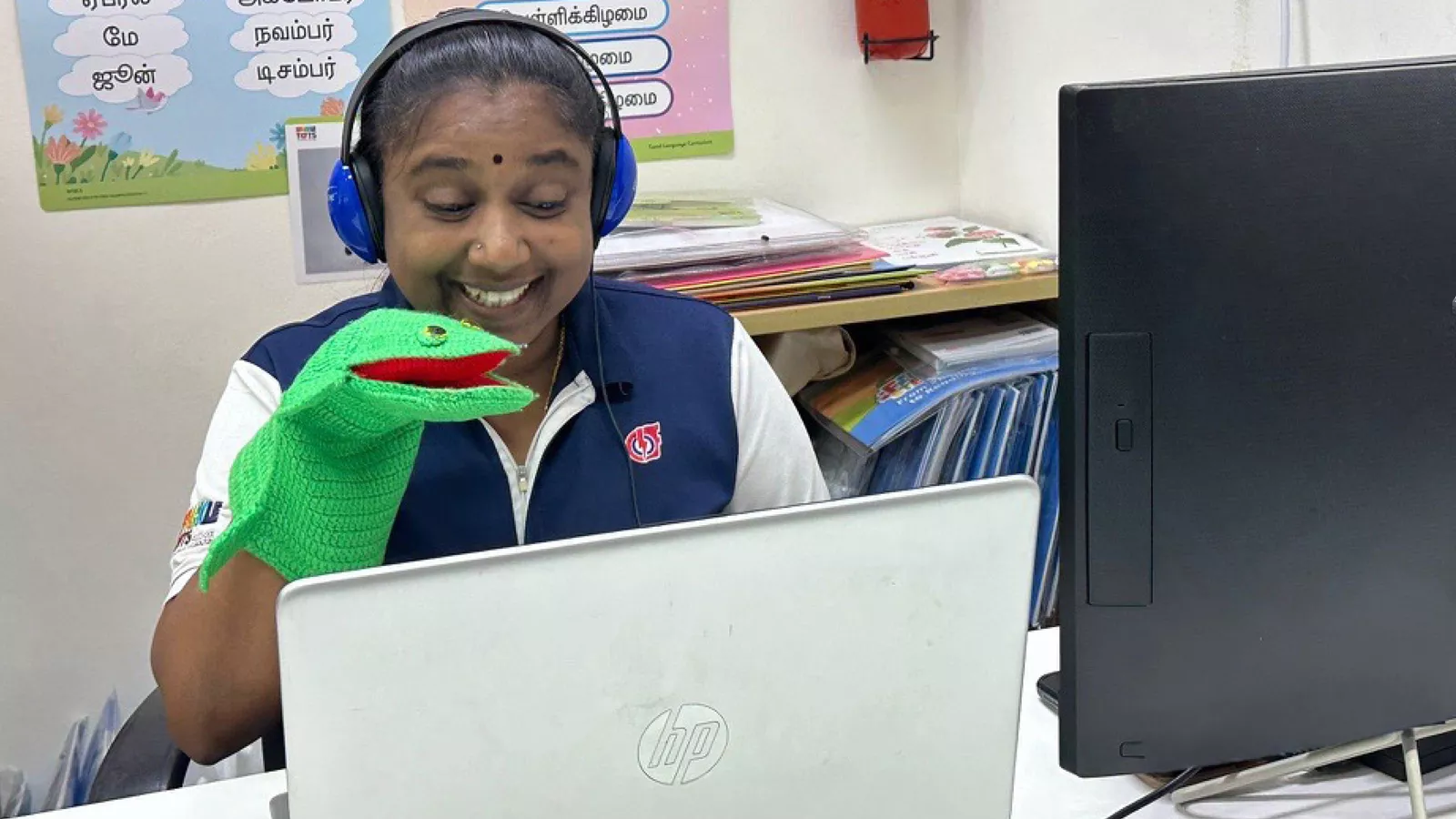 A Mother Tongue Language teacher conducts a virtual lesson, using a puppet and a Tamil poster to support storytelling.