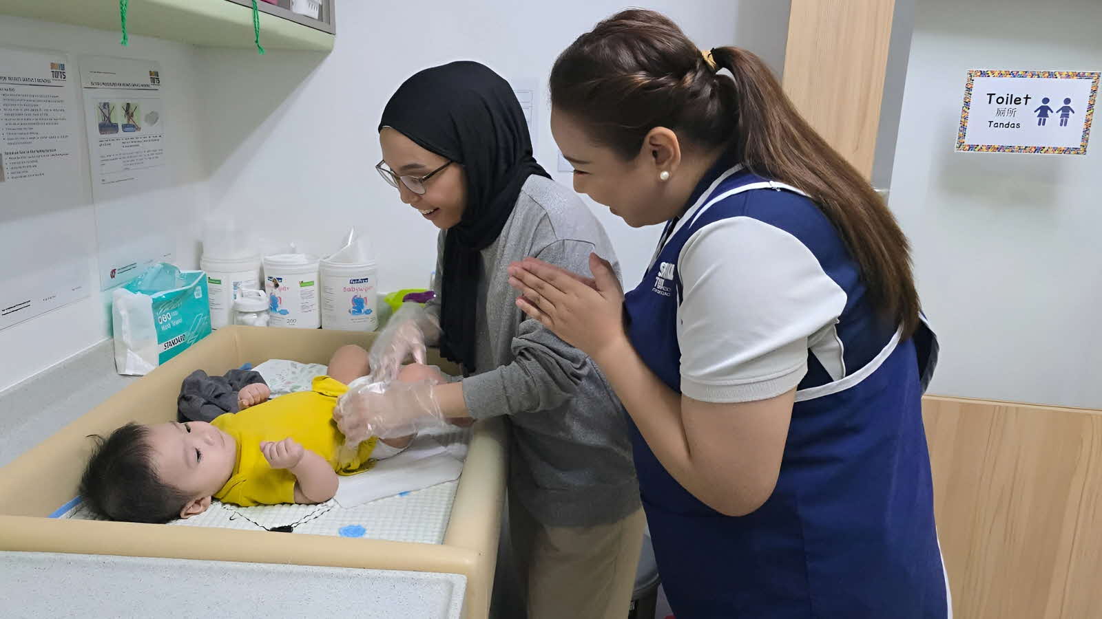 Two educators attend to a baby while changing diapers, demonstrating respectful, responsive and reciprocal interactions.