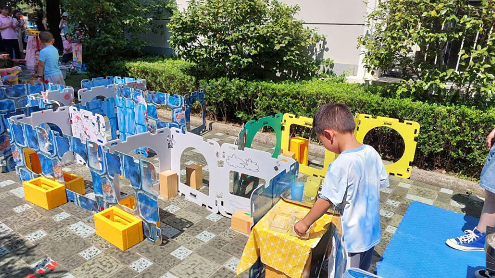 Children engage in outdoor play around a self-built maze constructed with various objects, having fun and showing agency.