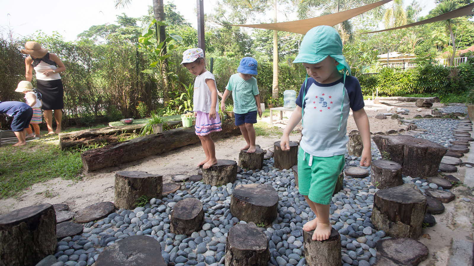 A group of children play on wooden stumps in an outdoor setting, engaging in true play and learning from the experience.