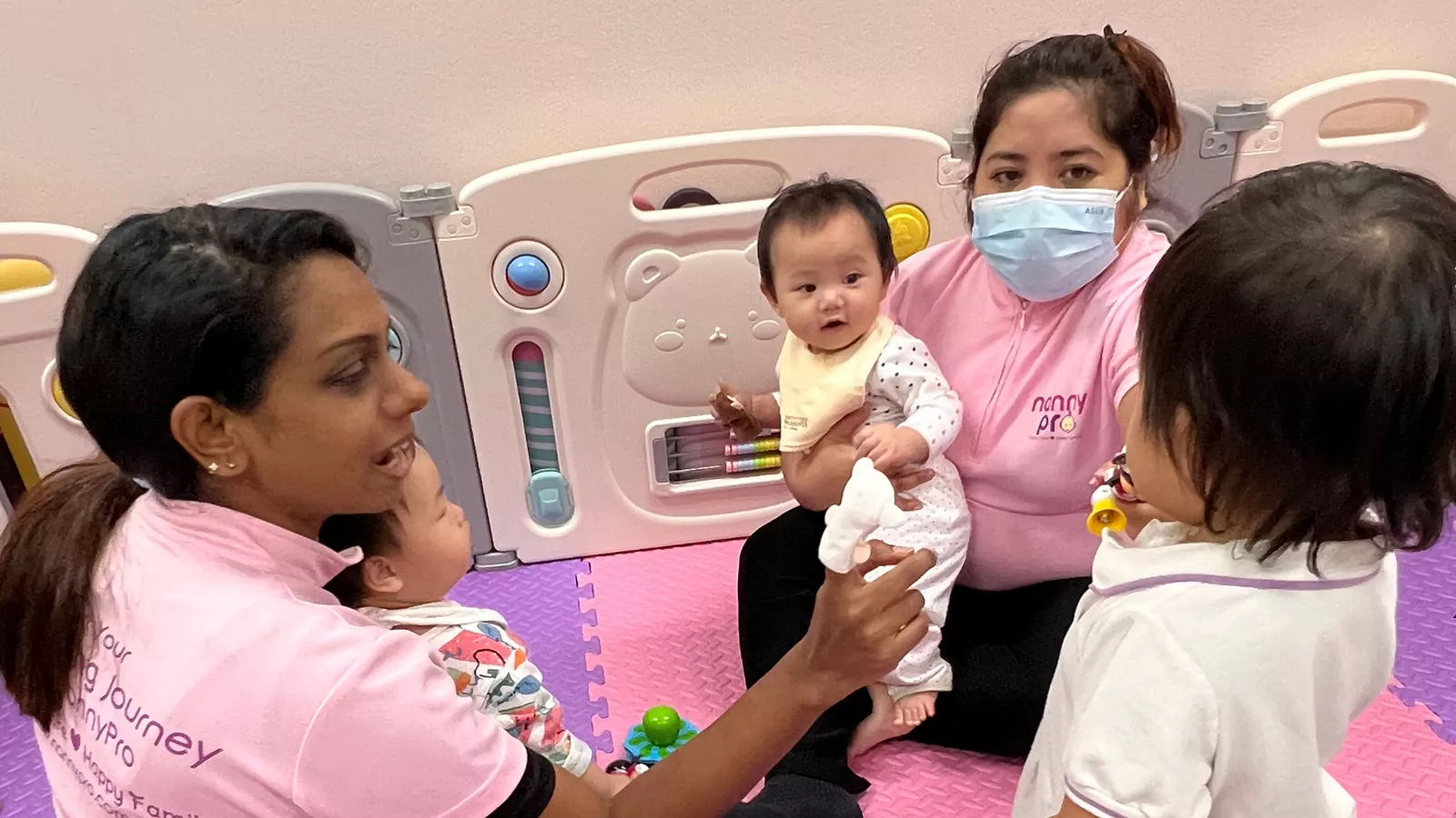 Two community-based childminders interact with three infants in a vibrant playroom, surrounded by toys and bright décor.