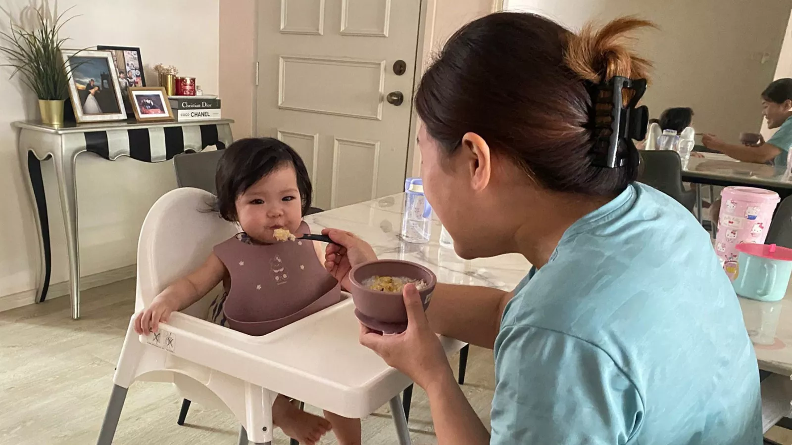 A childminder gently feeds a baby sitting in a high chair, illustrating the close bond between caregiver and infant.