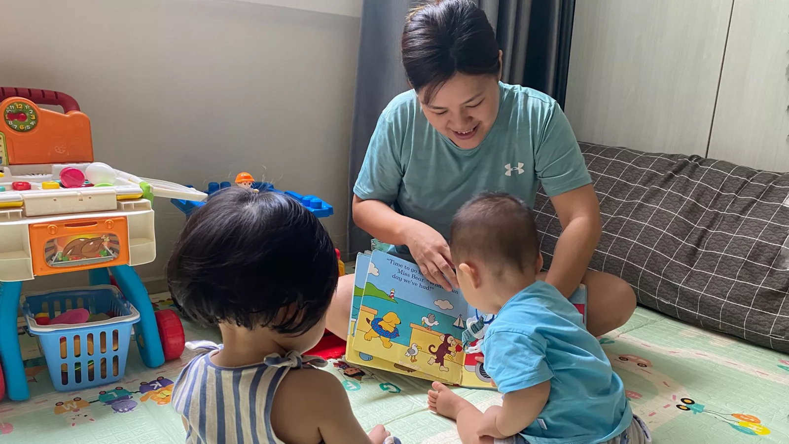 A childminder reads a story to two infants sitting on the floor, fostering a love for reading in a comfortable setting.