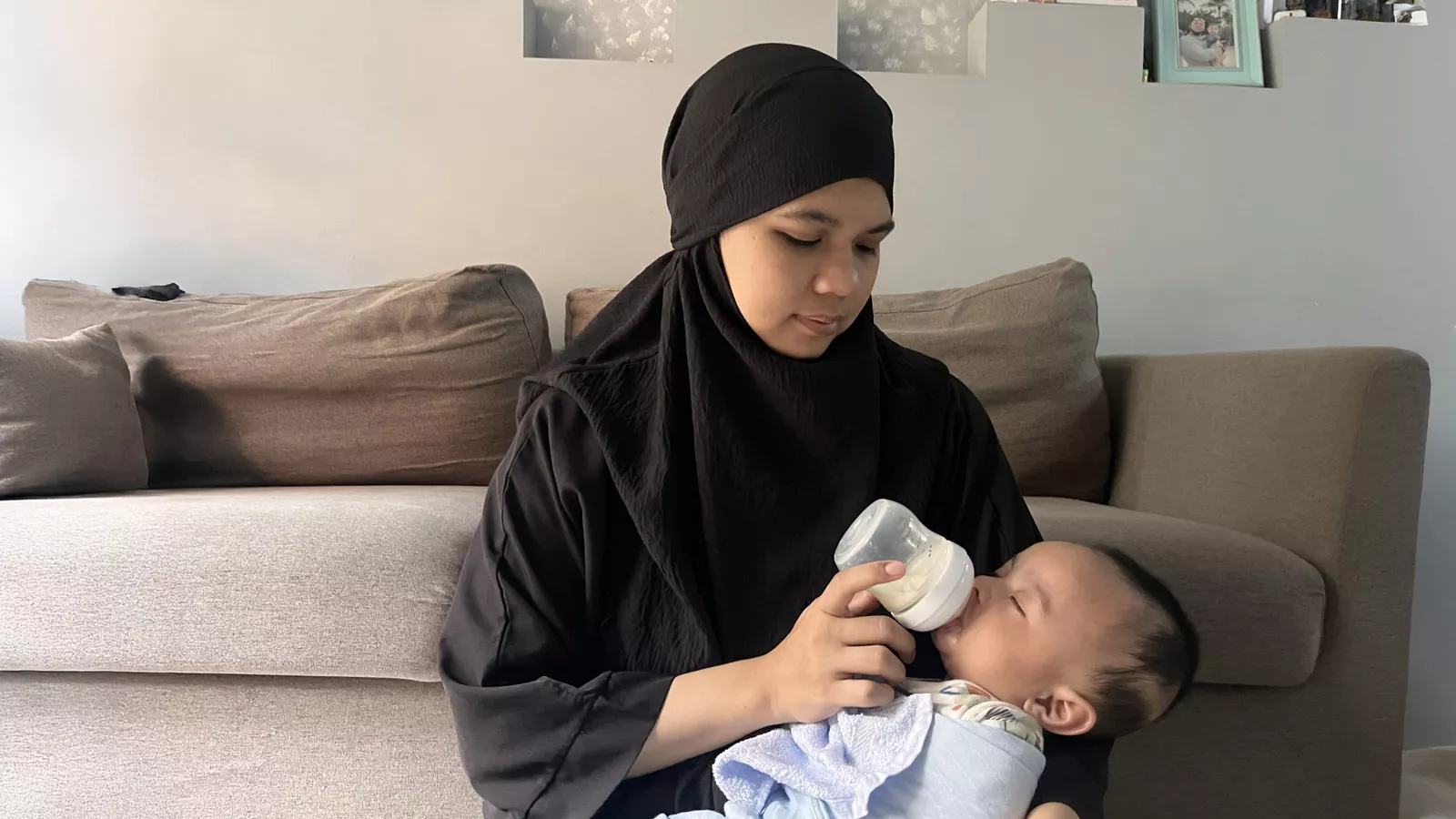 A childminder lovingly holds a baby as he drifts off to sleep after a nourishing bottle-feeding.