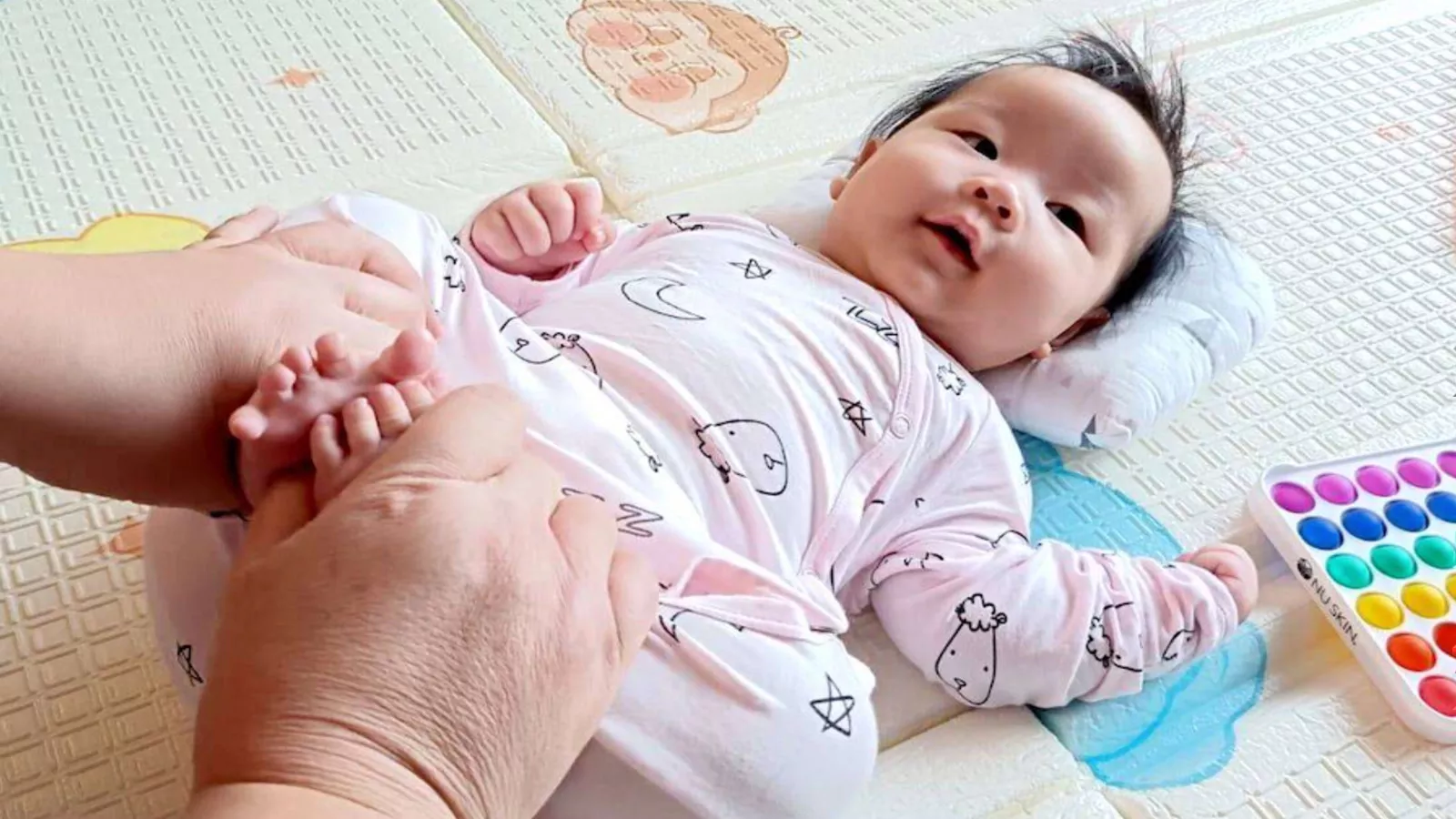 A baby lies on a mat while a person gently holds the baby’s feet, symbolising the loving care provided by a childminder.