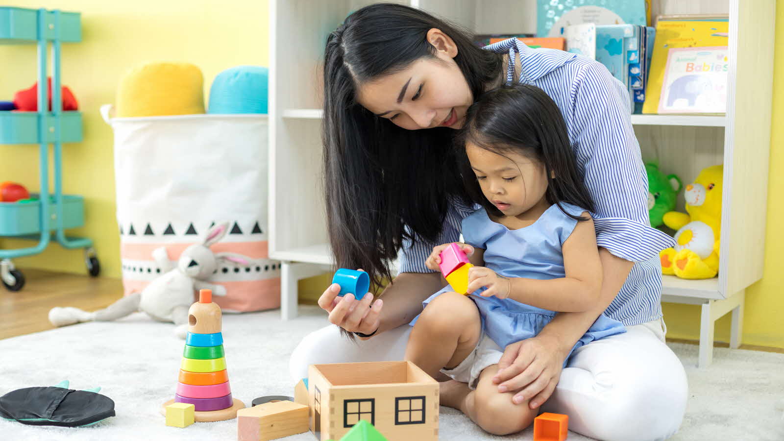 A woman and a child play with an assortment of toys on the floor, engaging in active play and enjoying their time together.