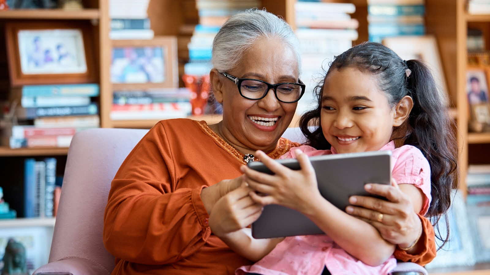 An older woman and a child look at a tablet together while sitting in a chair, demonstrating active screen use.