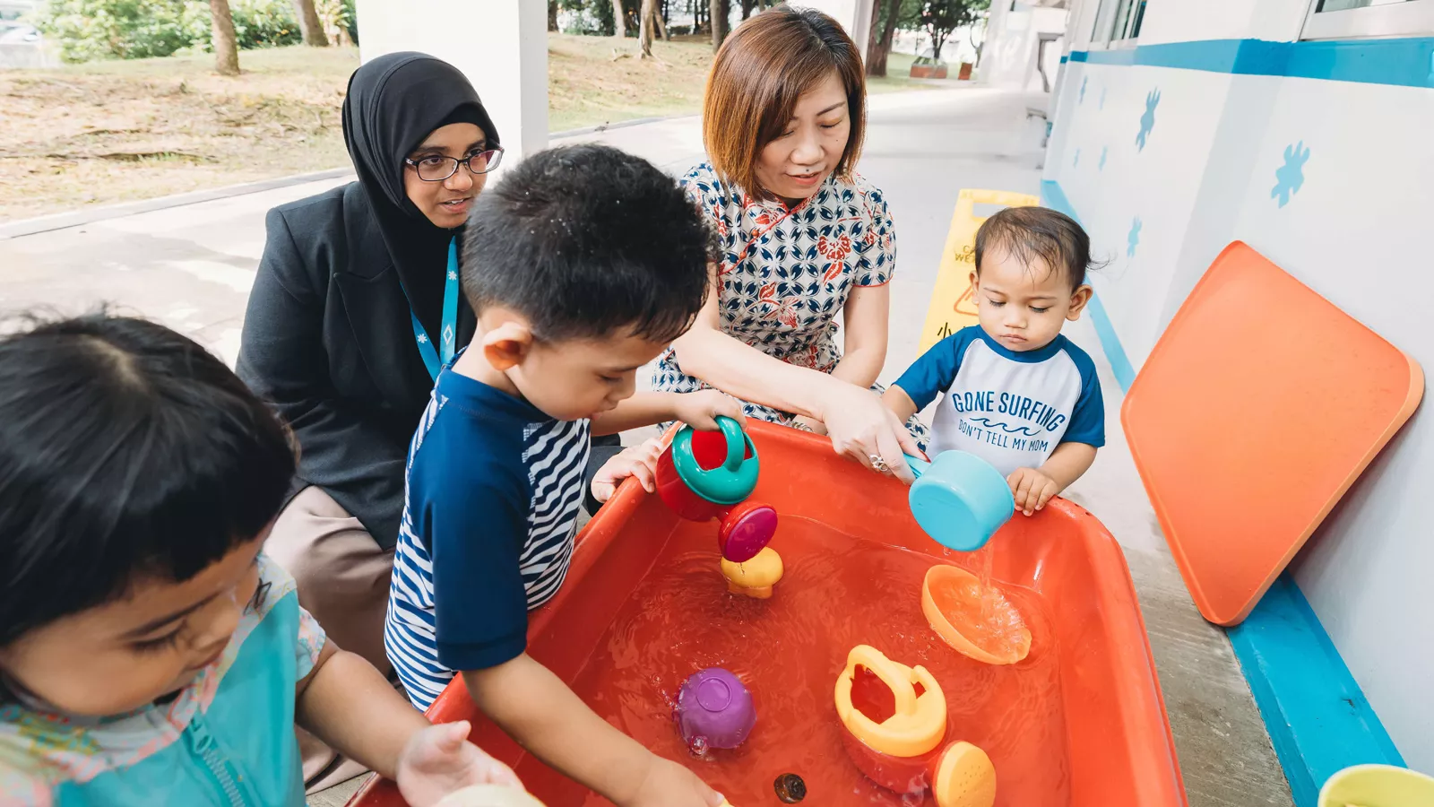 Ku Geok Boon interacts with children during a water play activity in a preschool setting.
