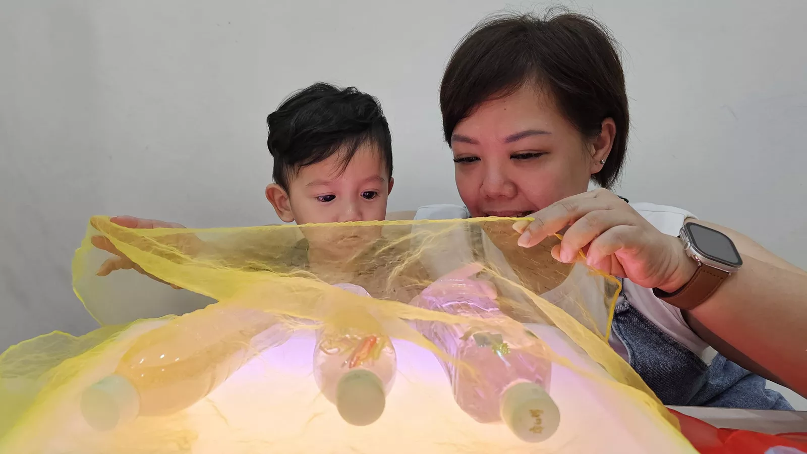 An infant educator engages a child in a sensory play activity involving a light box and various sensory bottles.