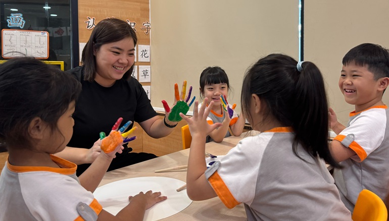 Educator engaged in hand painting activity with children