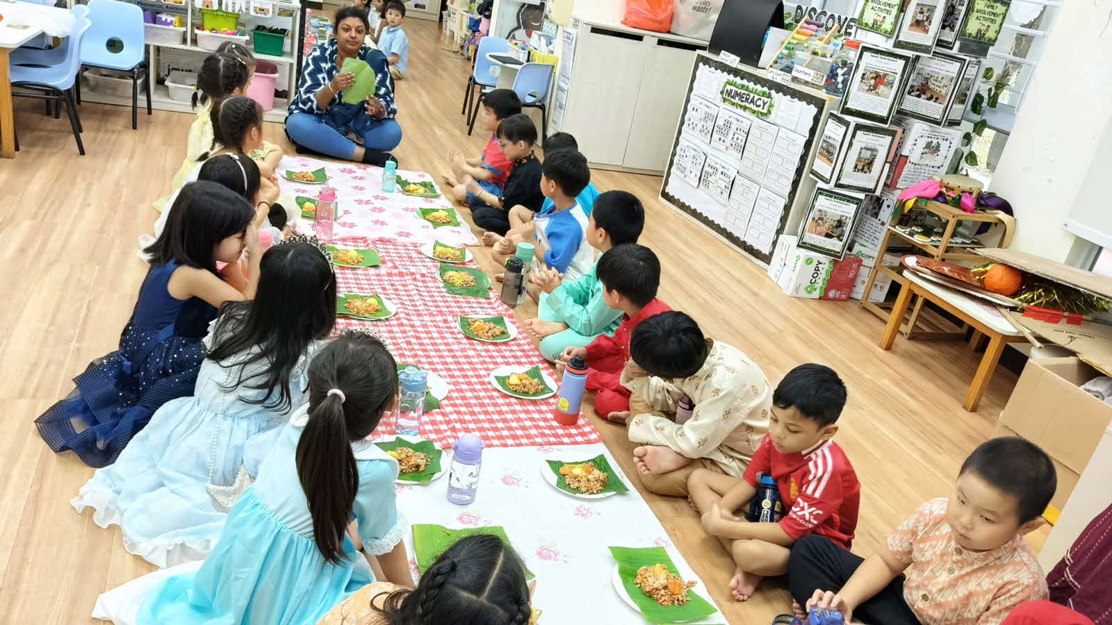 A group of children sit on the floor with plates of food in front of them, enjoying a meal together.