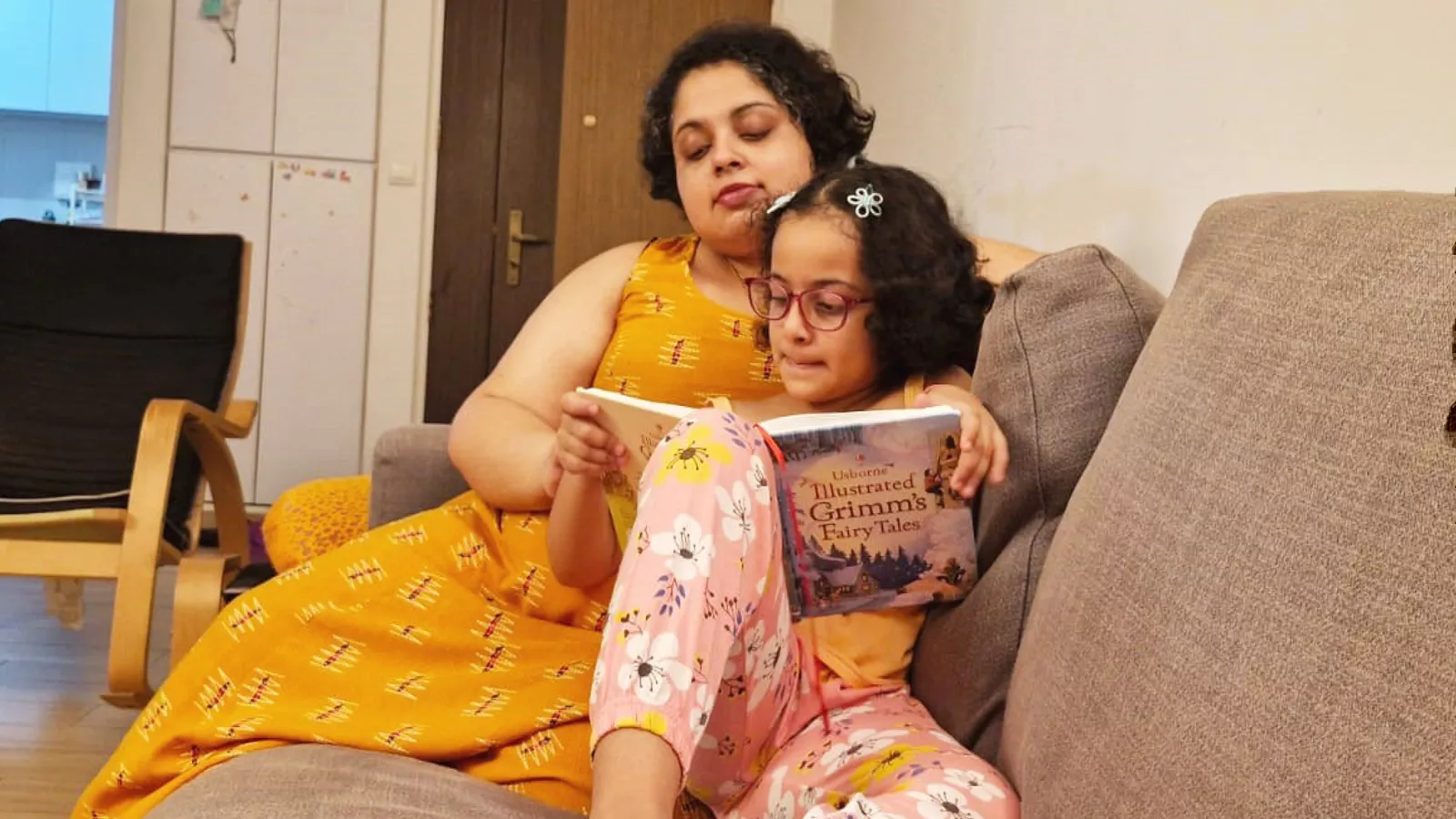 A parent and child sit on a couch and read a book together, focused on improving language and literacy skills.